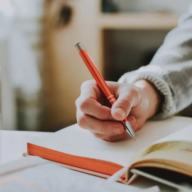 A learner writing practice answers in a notebook.
